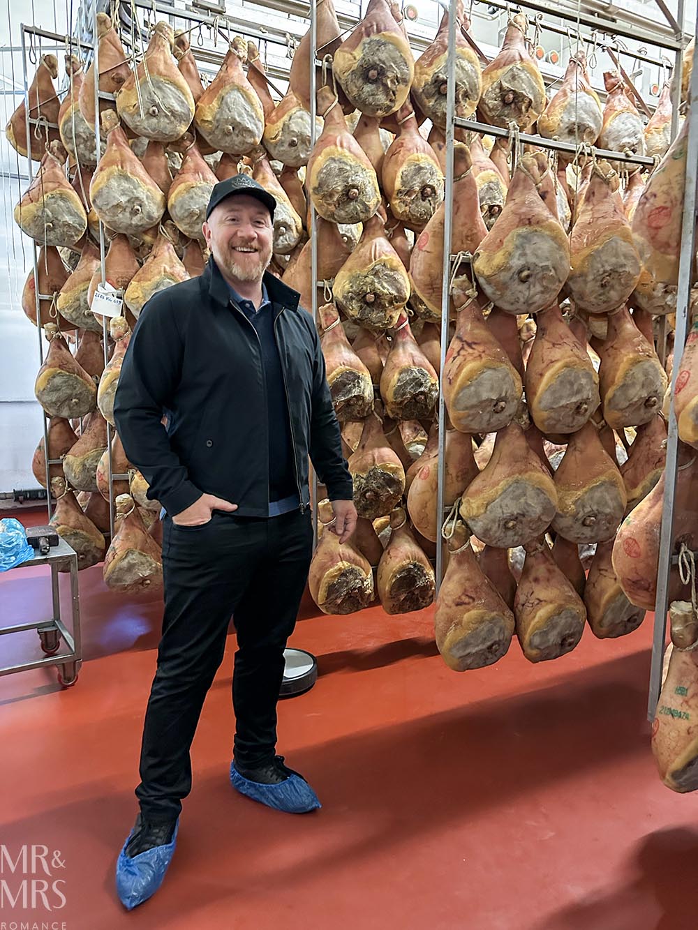 Jim next to prosciutto hams. Tour of parmegiano reggiano parmesan cheese and prosciutto di Parma in Parma Italy