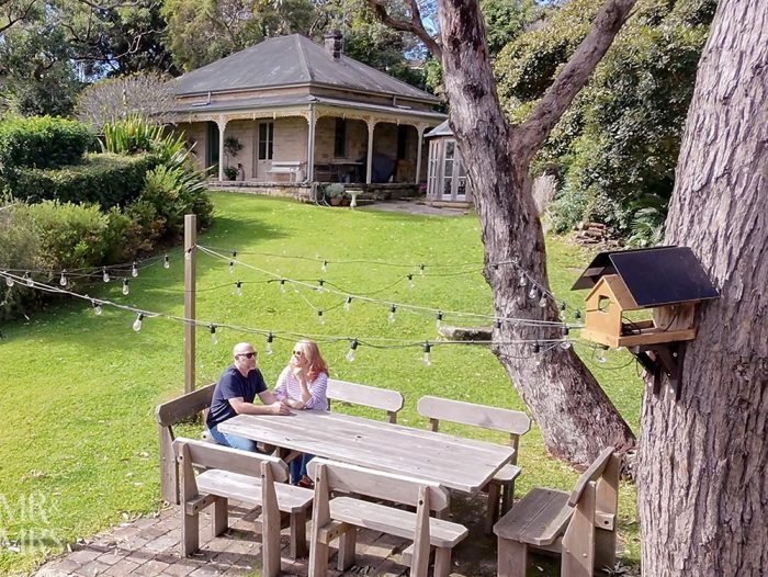 Simpson Cottage Review - view of cottage from garden table. Jim & Christina sitting at table