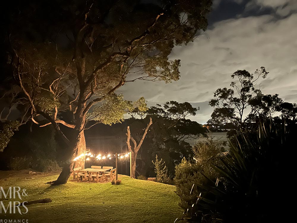 Simpson Cottage Review - cottage garden at night with lights above the garden table and the bay in the background