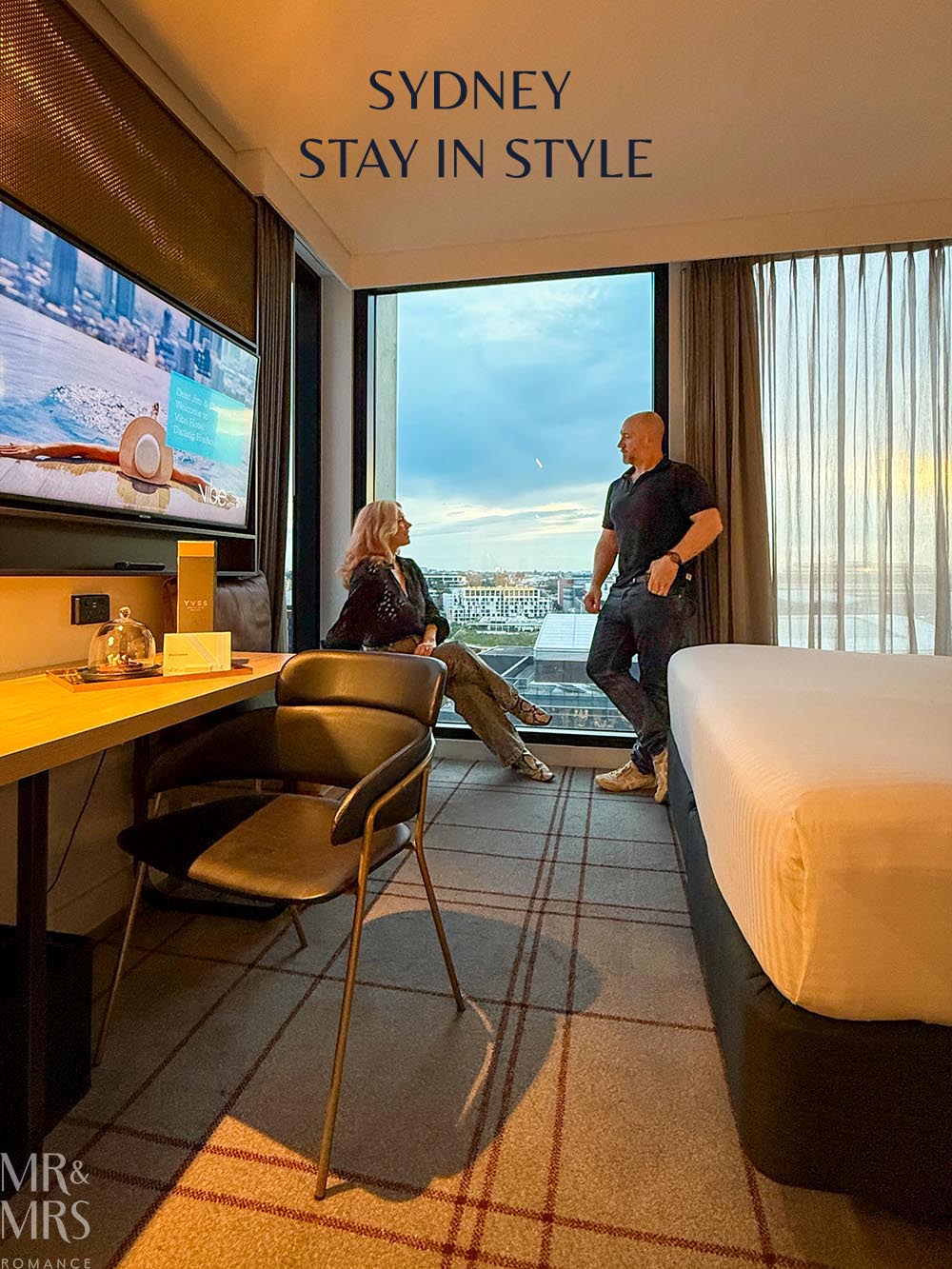 Vibe Hotel Sydney Darling Harbour review - Jim & Christina in front of the window of their suite. Title reads "Sydney Stay in Style".
